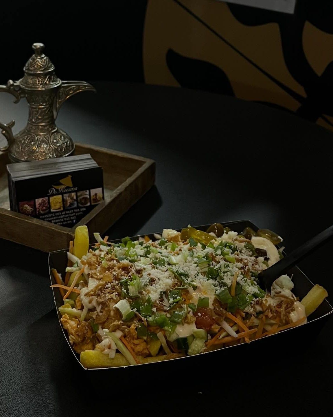 Loaded fries en een zilveren theepot op een donkere tafel